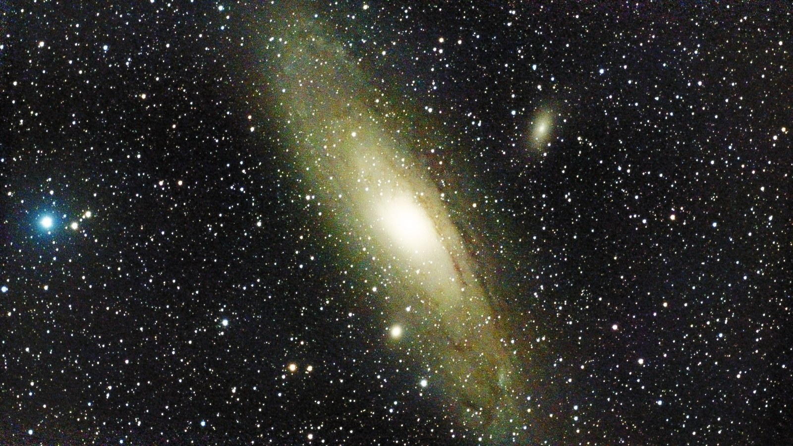 The Andromeda Galaxy, a tilted spiral with dark dust lanes across it, with its two companion galaxies visible as small ovals nearby.