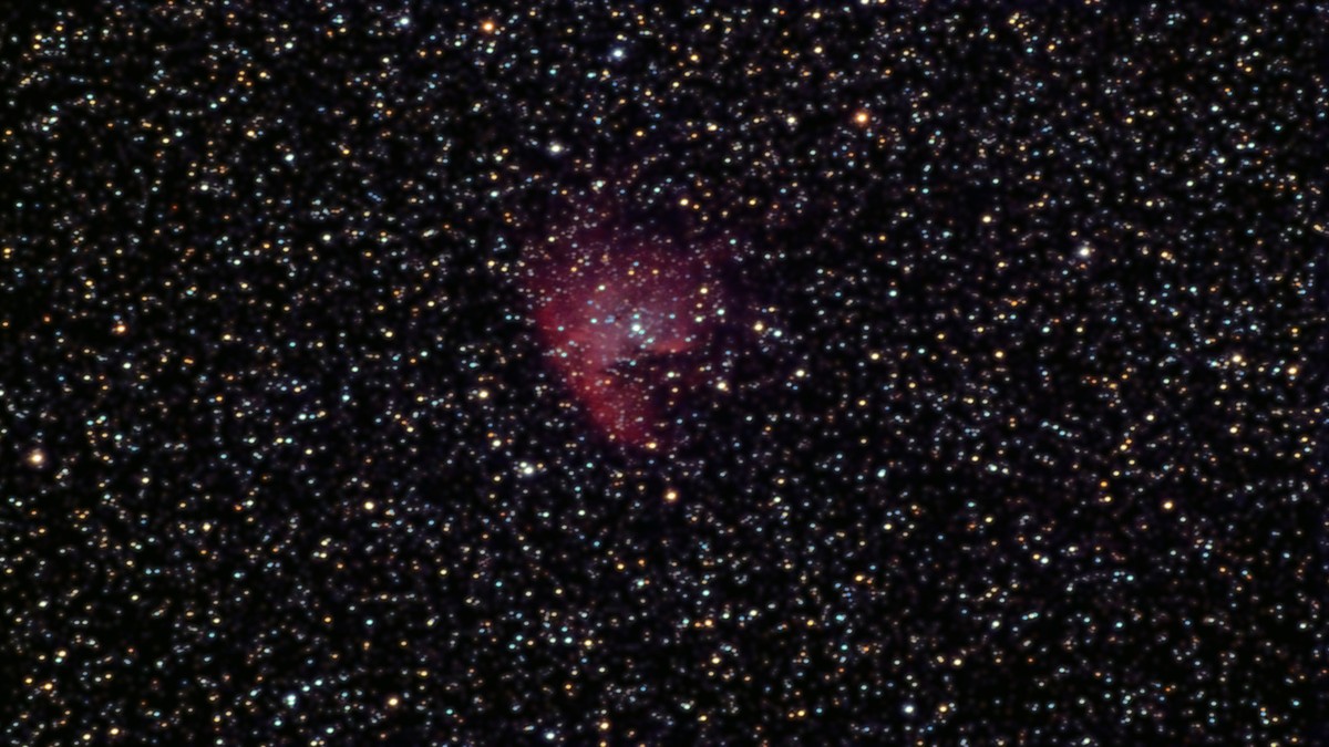 NGC 281, a rounded red nebula with a dark notch cut across it, set in a rich field of stars.