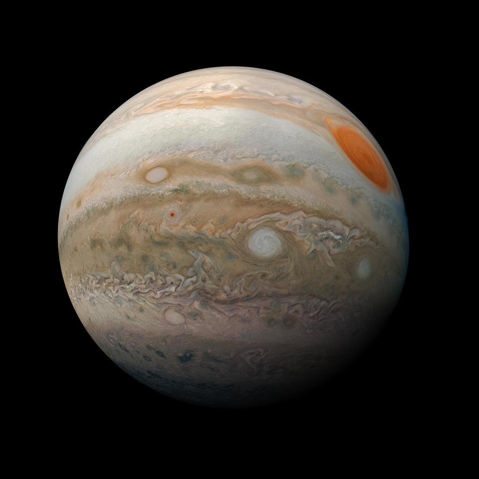 Jupiter photographed by the Juno spacecraft, showing banded cloud in cream and orange with the Great Red Spot near the edge.
